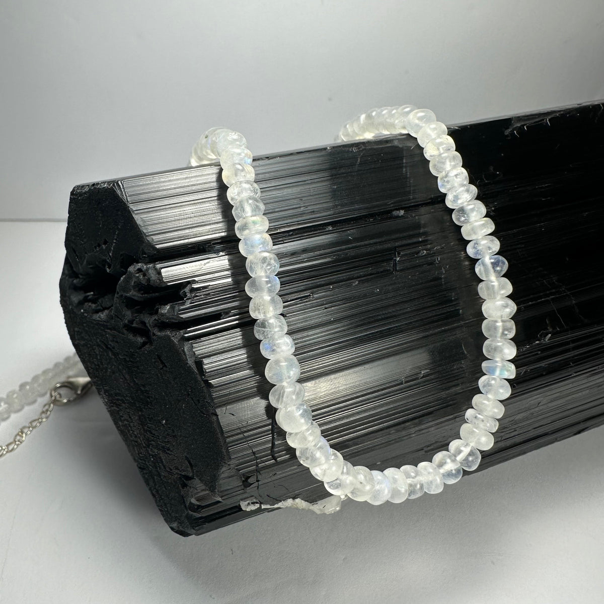 Close-up of translucent moonstone rondelle bead necklace draped over textured black tourmaline crystal on white background
