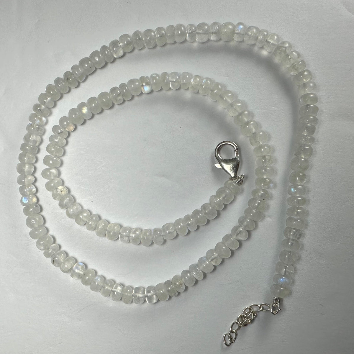 Coiled moonstone rondelle bead necklace with translucent white beads showing subtle blue flashes, finished with a silver lobster clasp and extender chain on a white background.