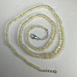 Graduated translucent Welo opal bead necklace with subtle yellow-green hues, silver lobster clasp, and extension chain, laid flat in a spiral on a white background.