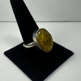 Silver ring with a large oval amber stone featuring natural inclusions, displayed on a black velvet ring stand against a white background.