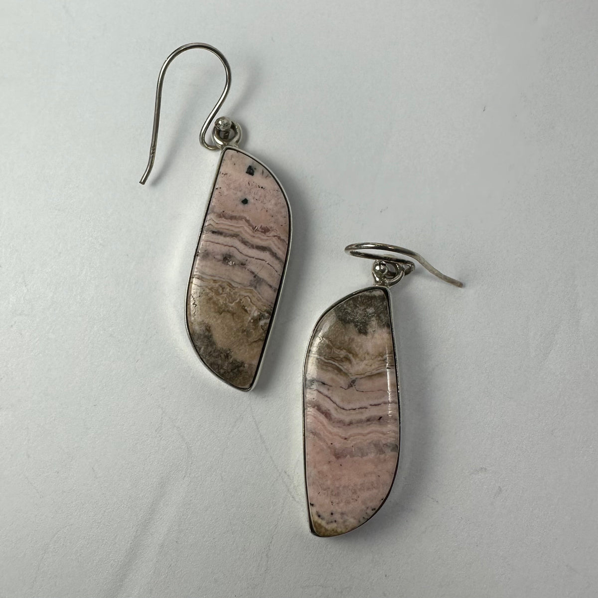 Pair of dangling rhodonite stone earrings with silver hooks, showing soft pink and beige tones with natural wavy patterns.