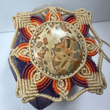 Handwoven flower-shaped necklace with concentric petals in cream, purple, and orange surrounding a round jasper stone with tan and brown patterns.