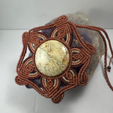 Hand woven necklace featuring a round beige jasper cabochon centerpiece with intricate brown macrame petals surrounding it, set on an amethyst crystal base.