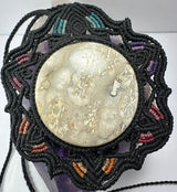 Circular jasper cabochon with beige and cream textures, set in a black hand-woven necklace featuring colorful thread accents in teal, purple, pink, and orange.