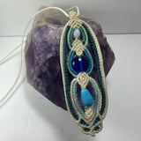 Hand-woven macrame necklace featuring glass beads and a 3.5 inch pendant displayed on fabric.