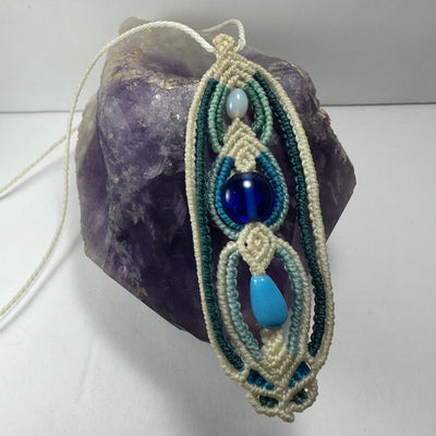 Hand-woven macrame necklace featuring glass beads and a 3.5 inch pendant displayed on fabric.