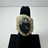 Oval black and white stone set in a cream-colored handwoven macramé band displayed on a black velvet ring holder.