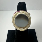 Handmade ring with a smooth round gray stone encircled by tightly woven cream-colored fiber on a black velvet display stand.