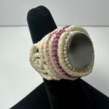Handmade woven ring featuring cream-colored and purple threads encircling a smooth, round gray stone, displayed on a black velvet ring stand.
