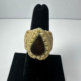Handmade beige woven ring with a glossy, smooth dark teardrop-shaped stone set in the center, displayed on a black velvet ring holder.