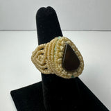Handwoven beige ring featuring a teardrop-shaped dark stone set in the center, displayed on a black velvet ring holder against a plain light background.