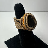Handwoven beige cord ring featuring a teardrop-shaped black stone centerpiece with an orange accent border, displayed on a black ring stand.