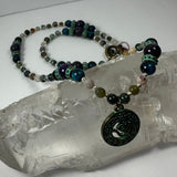 Bronze patina circular pendant with 'Om' symbol on a multi-colored beaded necklace resting on a translucent quartz crystal piece.