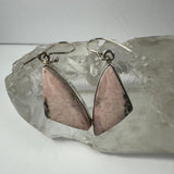 Pair of earrings with pink rhodonite stones set in silver, triangular shapes with natural black veining, displayed on a clear quartz cluster.