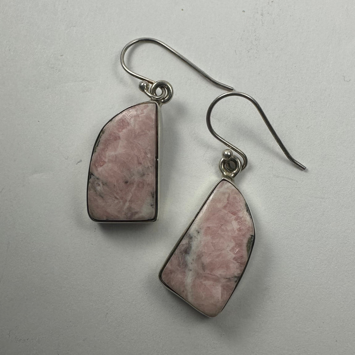 Pair of drop earrings featuring geometric rhodonite stones with pink and black marbled patterns set in silver-tone metal hooks against a plain light background.