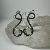 Pair of silver earrings with an elegant, curved 'S' shape design, each featuring a round moonstone set near the lower curve, displayed on a clear quartz crystal.