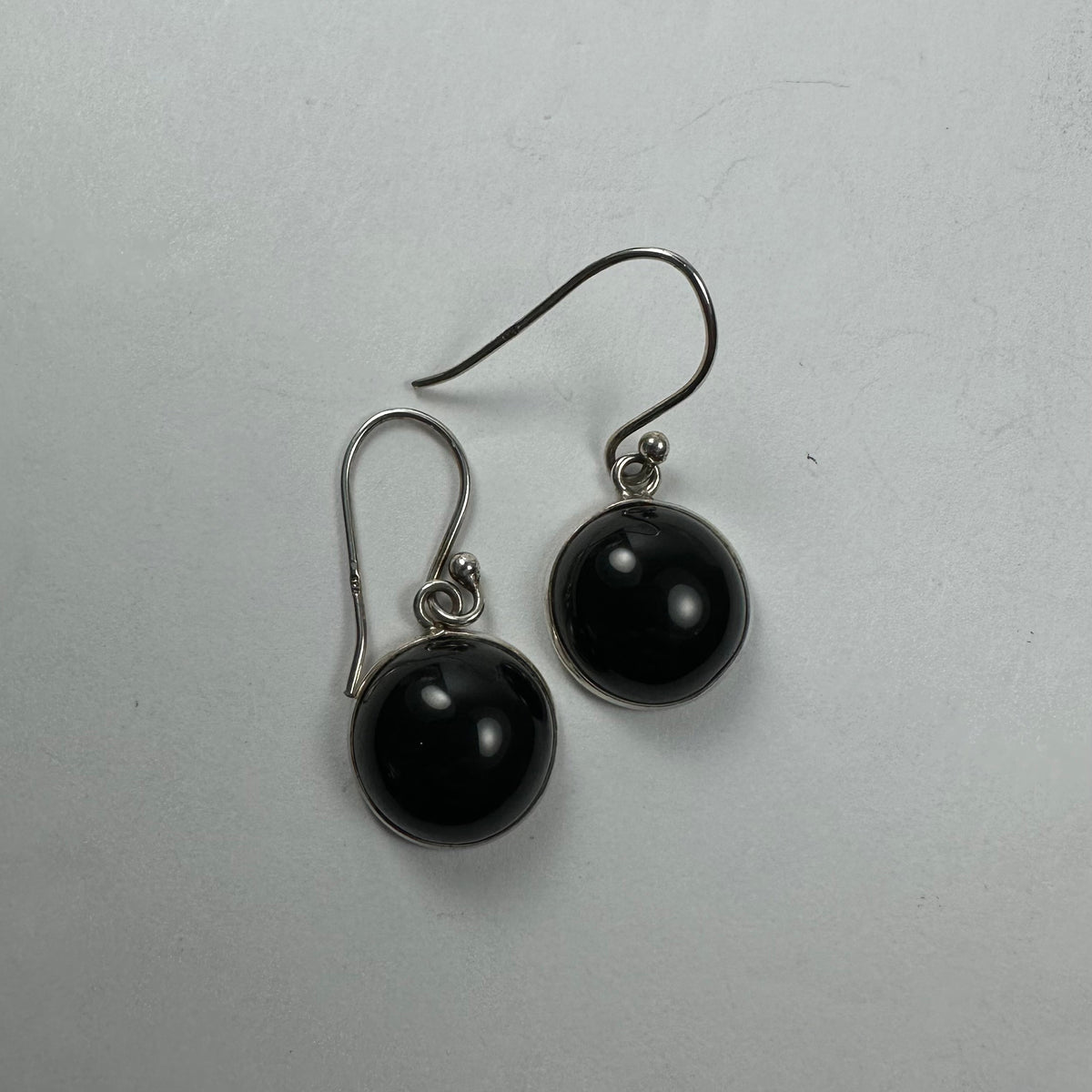 Pair of round black onyx drop earrings set in silver with simple hooks on a light gray background.