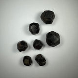 Seven dark red faceted natural almandine garnet crystals with dodecahedral shapes on a neutral light background.