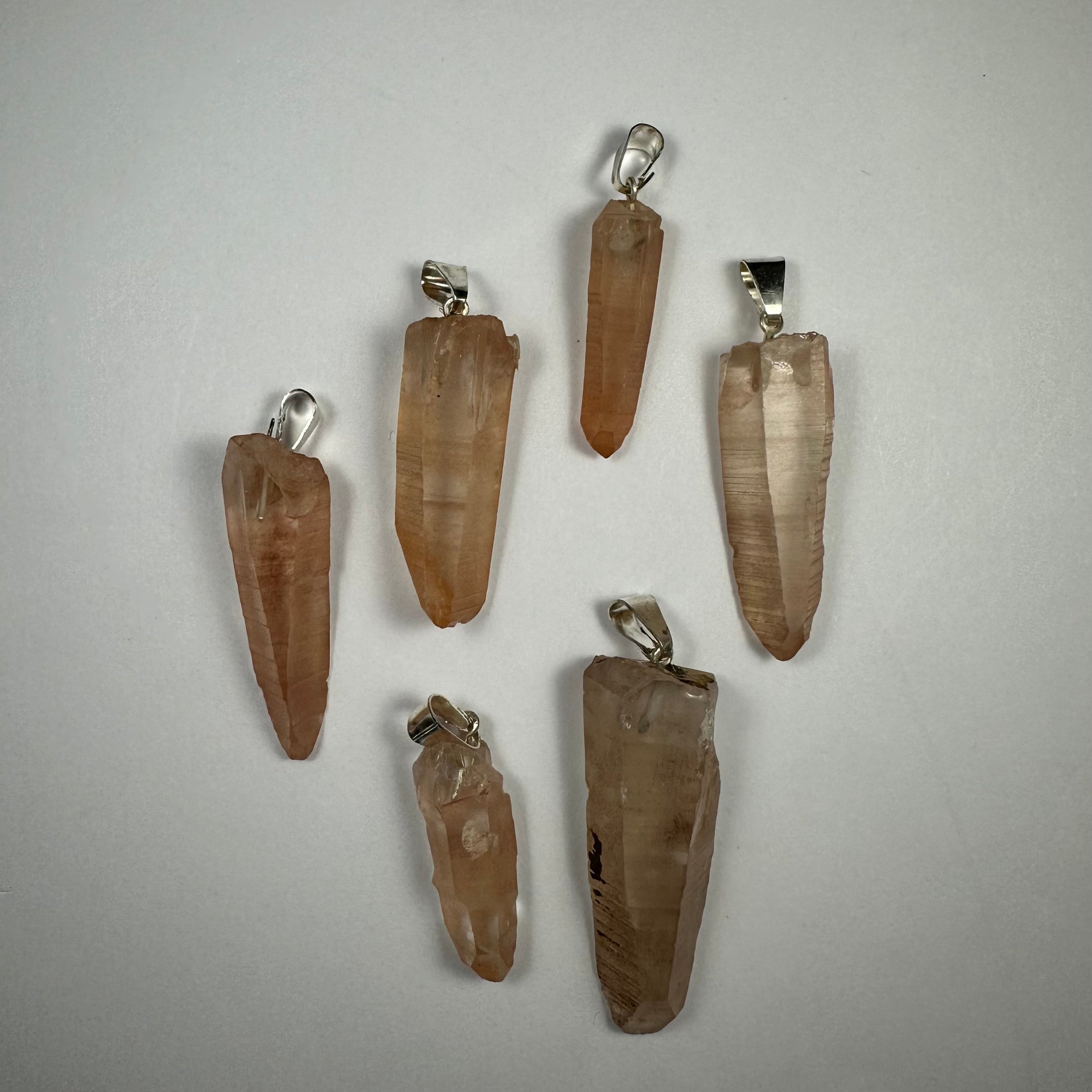 Assorted crystal pendants from Rare Earth Gallery featuring natural quartz points and wire wrapped designs on neutral backgrounds