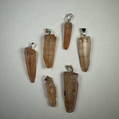 Assorted crystal pendants from Rare Earth Gallery featuring natural quartz points and wire wrapped designs on neutral backgrounds