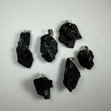Six irregularly shaped black crystal pendants with silver bails arranged on a plain light gray background, highlighting their glossy and textured surfaces.
