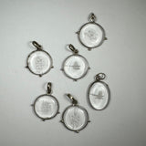Six round and oval clear crystal pendants with various abstract and symbolic carvings, each set in simple metal frames with small loops for hanging.