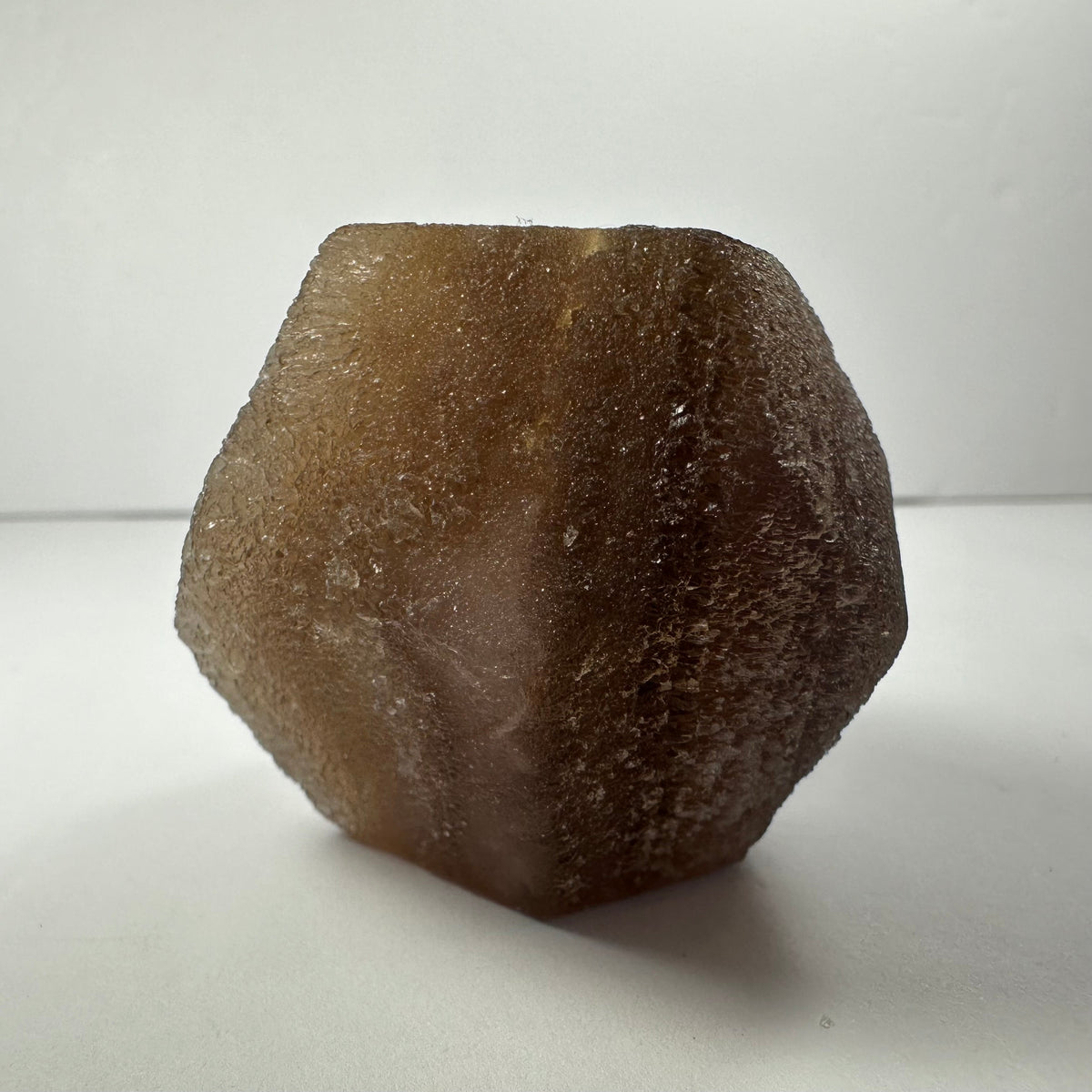 Brown, translucent fluorite dodecahedron with a textured surface, displayed upright on a white background with subtle shadowing.