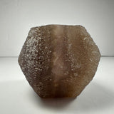 Hexagonal brown fluorite dodecahedron with textured, crystalline surfaces and a gradient from dark to light brown, displayed against a plain white background.