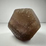Brown translucent fluorite dodecahedron crystal with rough, textured surfaces shown against a white background.