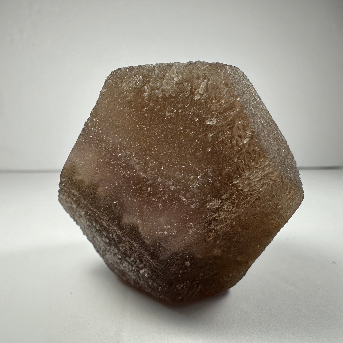 Brown translucent fluorite dodecahedron crystal with rough, textured surfaces shown against a white background.