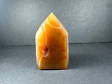Polished, pointed tower-shaped stone with warm orange and yellow banded patterns and a small rough patch, displayed against a gray background.