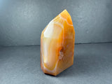 Polished banded carnelian tower standing upright with orange, white, and reddish-brown layers and a small rough-textured inclusion on one side.