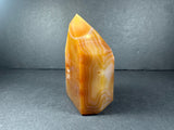 Polished orange and cream banded carnelian tower with distinct layered patterns, standing upright against a dark gray background.