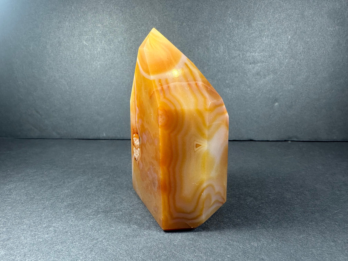 Polished orange and cream banded carnelian tower with distinct layered patterns, standing upright against a dark gray background.