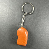 Keychain with an irregularly shaped smooth orange mixed stone attached to a silver metal chain and keyring on a gray background.