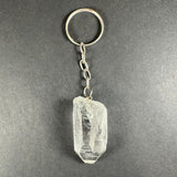 Clear rough-cut crystal pendant attached to a small silver chain and round keyring on a dark gray background.