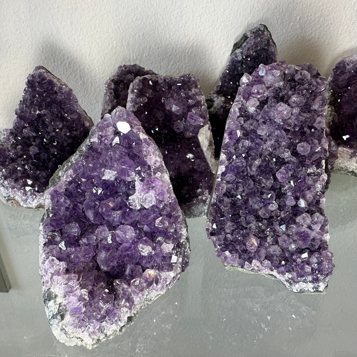Several irregularly shaped clusters of purple amethyst druzy crystals with varying sizes and vibrant faceted surfaces on a reflective gray surface.