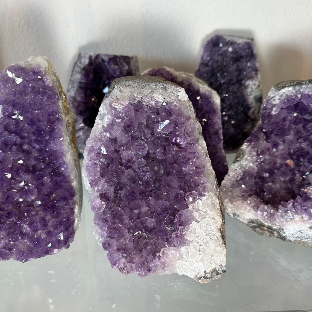 Close-up of several large amethyst crystal geodes with deep purple clusters and white outer edges, displayed upright against a light background.