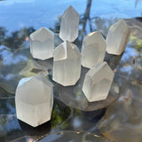 Seven translucent white selenite obelisks with polished faceted sides and pointed tops arranged on a glossy, multicolored agate surface reflecting natural light.