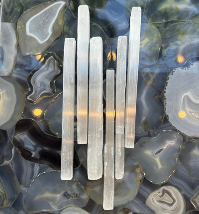 Rough white selenite bar resting on a dark textured surface, showing natural striations and a matte finish
