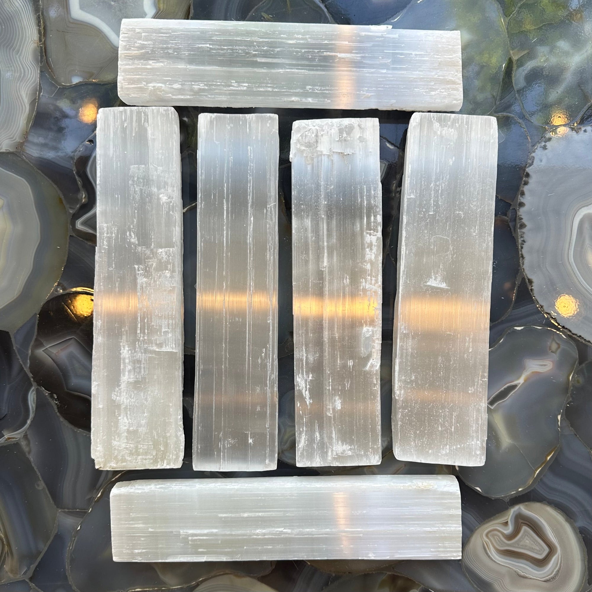 Three rough selenite bars showing white translucent striated mineral texture on a neutral background