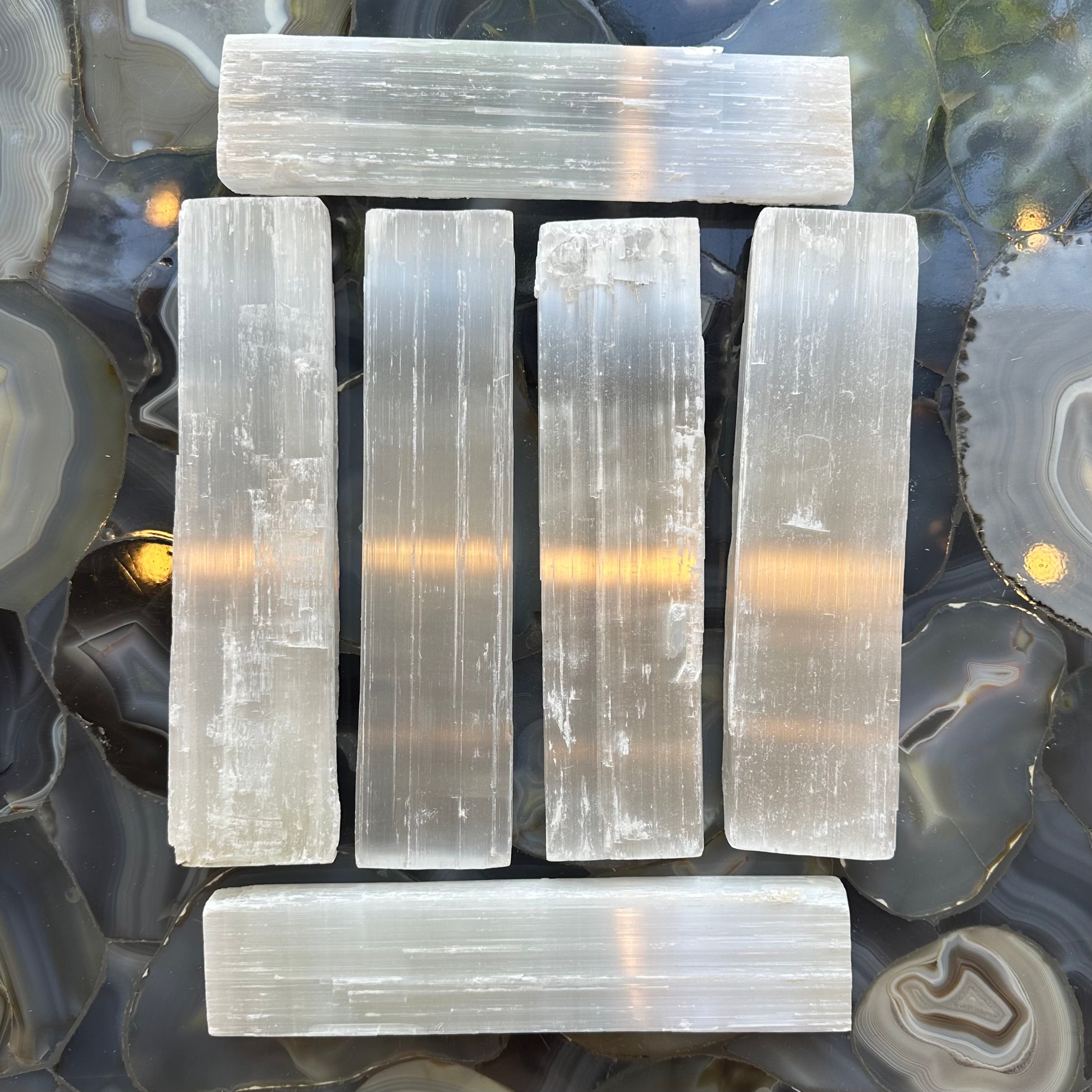 Three rough selenite bars showing white translucent striated mineral texture on a neutral background