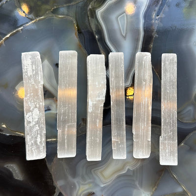 Rough selenite stick approximately 15cm long with natural textures, displayed on a light surface.