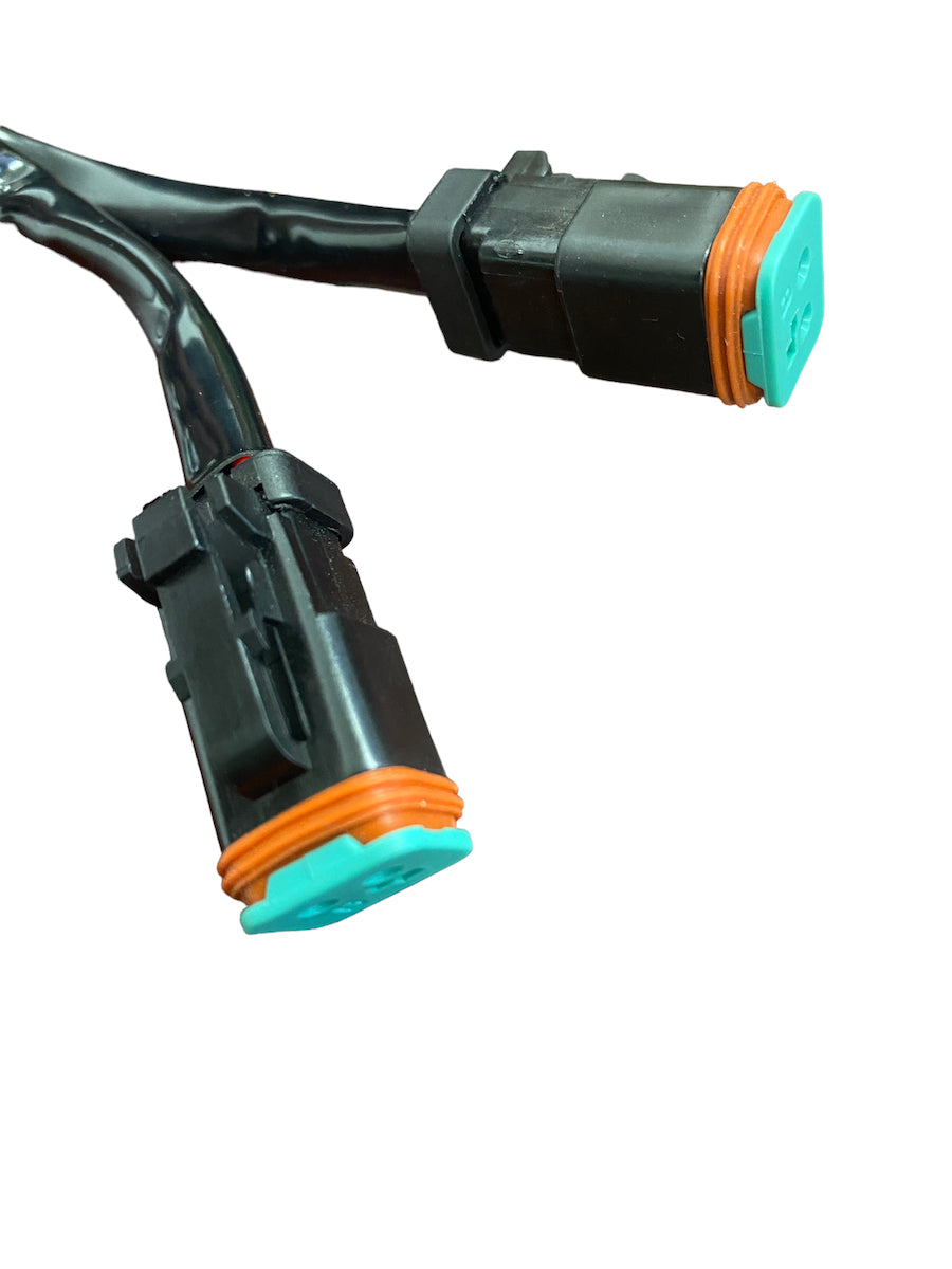 Close-up of black dual Deutsch electrical connector with turquoise and orange sealing components on black wires, isolated on white background.