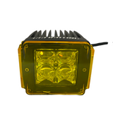Square black LED pod light with a yellow transparent lens cover and four individual bulb lenses visible inside, connected by a black power cable.