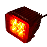 Compact black LED pod light with red colored lens cover and multiple bright yellow LED bulbs inside, shown angled with cooling fins on top and side controls.
