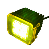Compact black LED pod light with a translucent yellow colored cover glowing softly, showing cooling fins on top and side screws securing the cover.