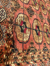 Vintage Turkoman Tekke rug with repeating geometric floral motifs in warm reds, browns, and cream tones, showing a slightly worn textured surface.