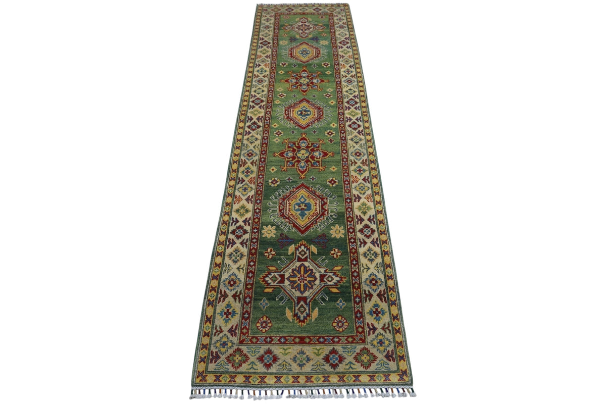 Long narrow hand-knotted Afghan Kazak wool rug with a green field, geometric medallions, floral motifs, and cream borders with intricate patterns and tassels.