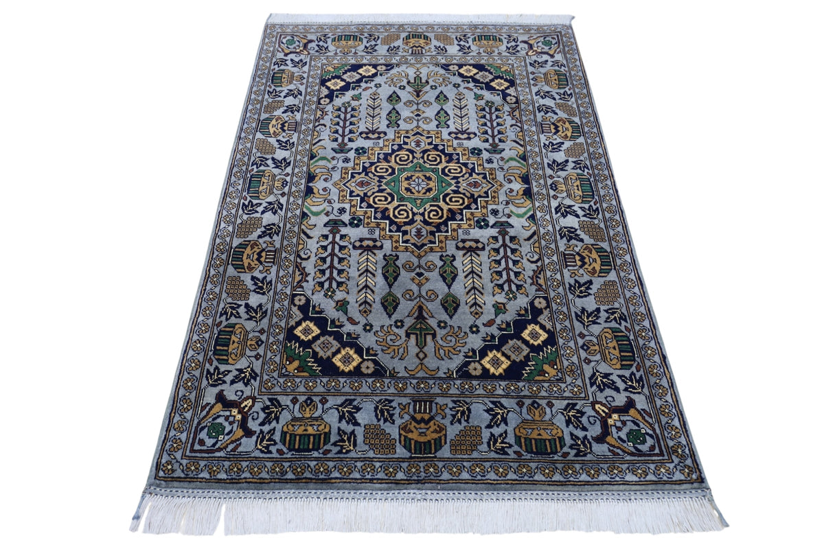 Rectangular hand-knotted Afghani Zerkhaki wool rug with a central medallion in navy, green, and mustard on a pale blue background, featuring floral and geometric patterns and white fringes.